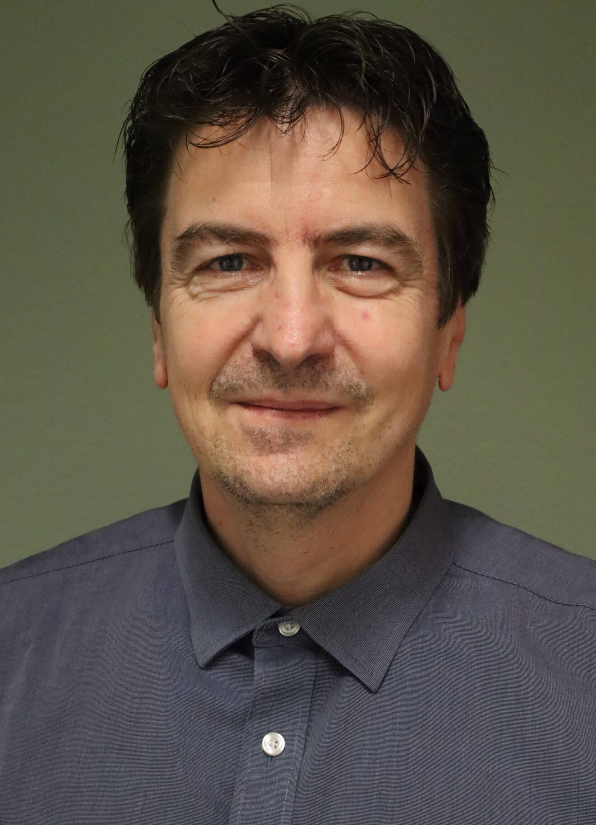 Porträt eines Mannes in einem blauen Hemd mit freundlichem Ausdruck, grüner Hintergrund.